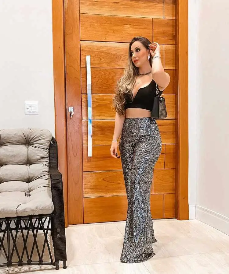 Mulher com calça brilhosa e top preto.