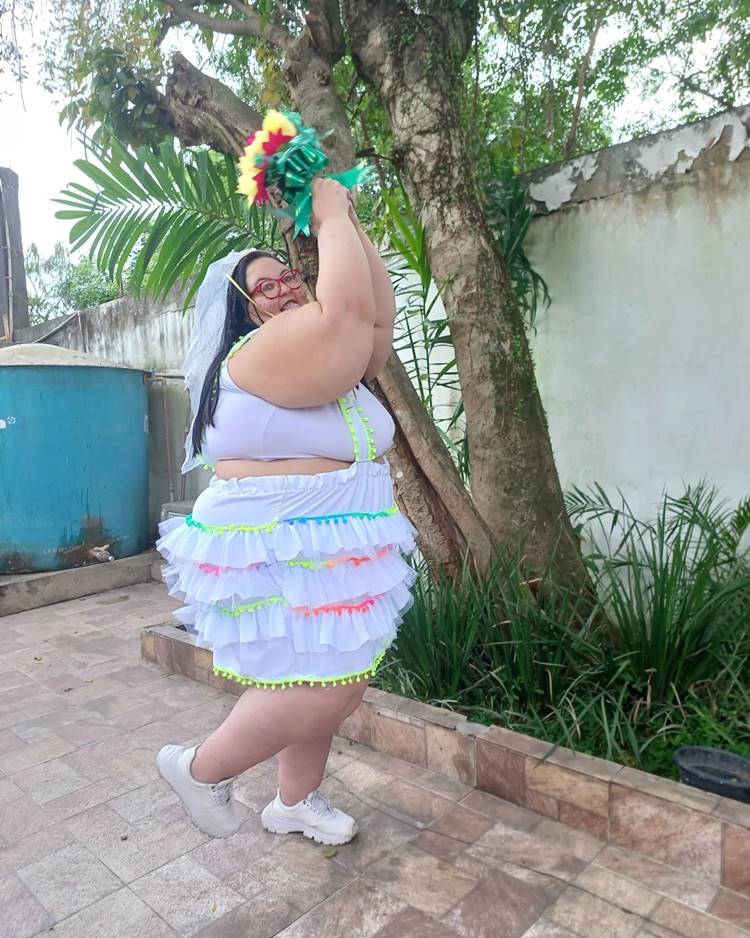 Noiva caipira com vestido branco com detalhe de pompom, ela segura buquê no alto