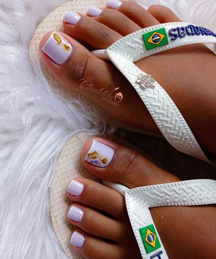 Pé de pessoa de pele negra com francesinha nas unhas e flor no dedão