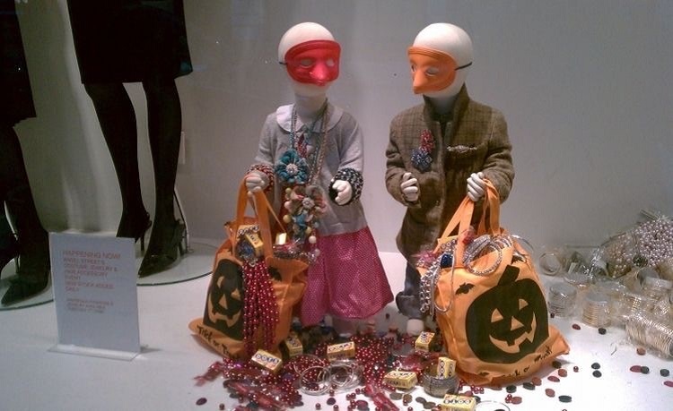 Vitrine de loja infantil para o Dia das Bruxas com manequins fantasiados, com sacolas de abóboras 