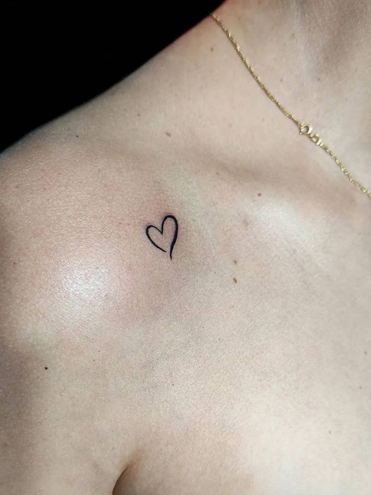 Mulher de pele clara com corrente de dourada e contorno grosso de coração tatuado no ombro