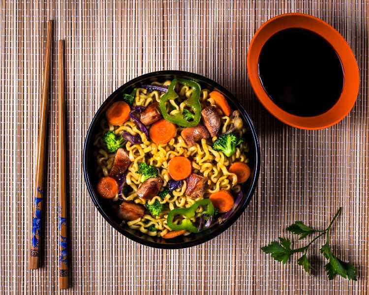 yakisoba de frango e legumes em mesa com shoyo e hashi