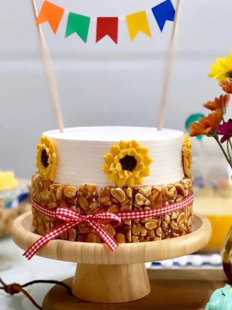 Bolo branco enfeitado com varal de bandeirinhas, flores e pé de moleque 