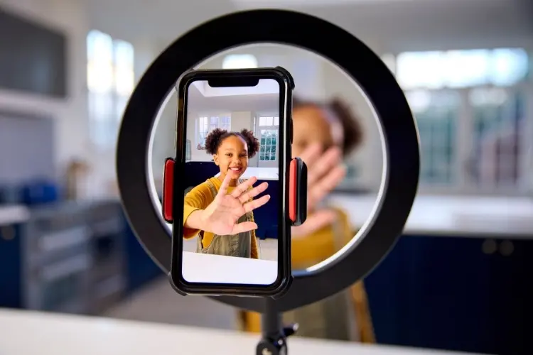 Criança de pele negra acenando para celular aberto na câmera e ring light