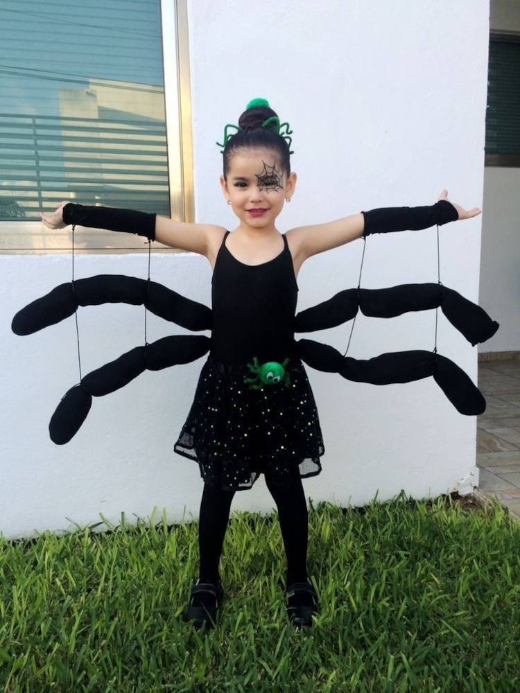 Criança de pele clara com blusa preta, caia preta com brilho e pernas de aranha 
