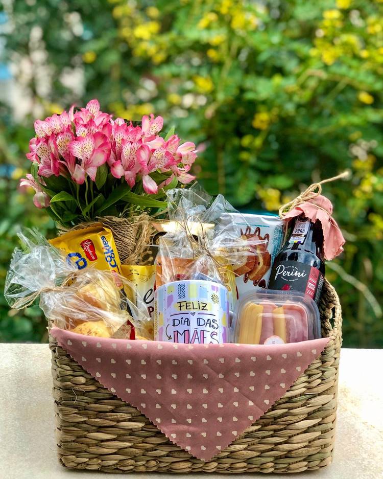 Cesta de Dia das Mães com docs, biscoitos, pães, suco de uva, frios, caneca Feliz Dia das Mães e flor