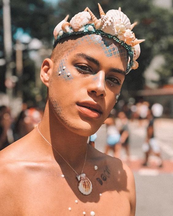 Homem de pele morena com maquiagem de sereia e coroa de conchas