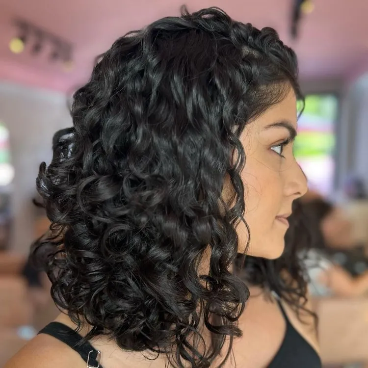 Uma mulher cacheada de cabelo preto, posando de perfil, com cabelos na altura do ombro