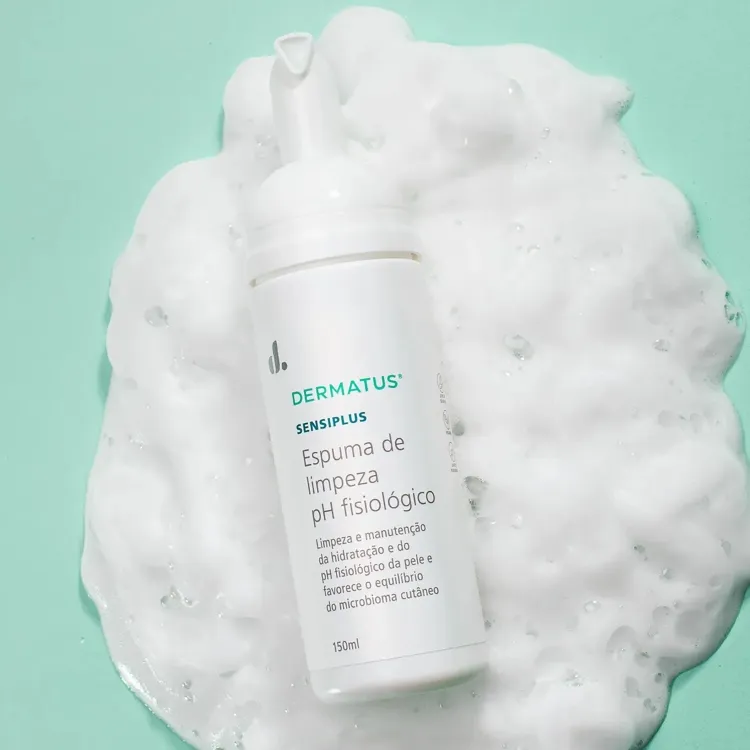 A imagem exibe um frasco branco de "DERMATUS SENSIPLUS Espuma de limpeza pH fisiológico", envolto por uma rica espuma branca, sobre um fundo verde-claro. O rótulo destaca "limpeza e manutenção da hidratação e do pH fisiológico da pele" e o volume de 150ml.







