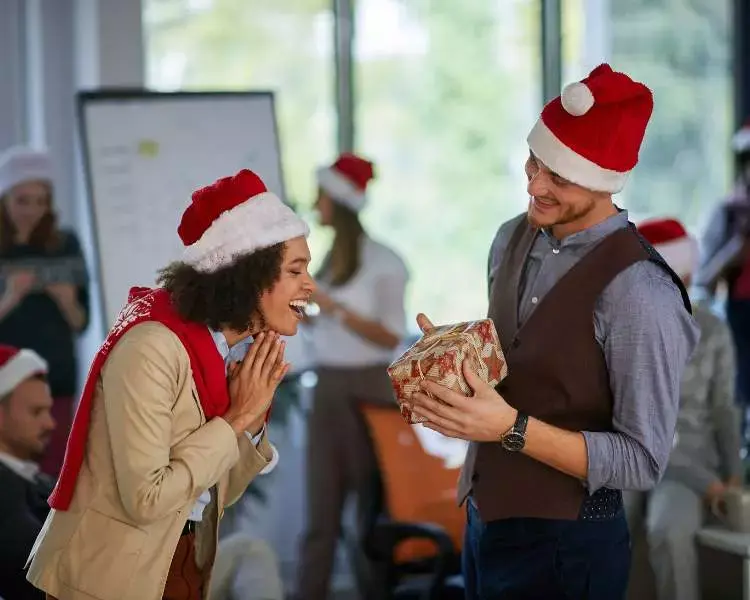 Mulher de pele escura e homem de pele clara usando gorro de papai noel em amigo secreto de empresa