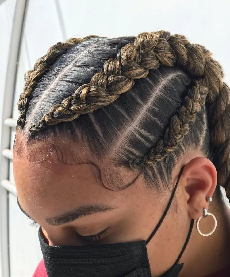 Trança nagô embutida grande em cabelo natural. Mulher usa máscara e brincos prateados