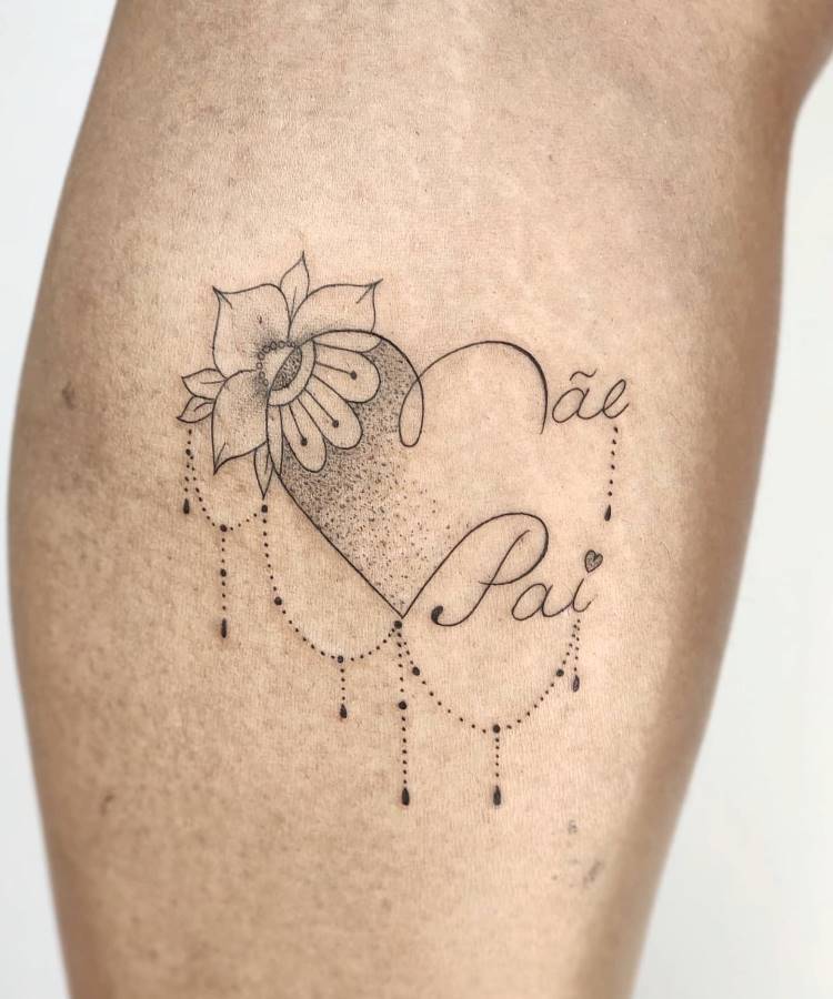 A imagem apresenta uma tatuagem detalhada na perna de uma pessoa, com um coração sombreado por pontos. Uma flor delicada brota do topo do coração, enquanto a parte inferior é adornada com linhas pontilhadas e pingentes. As palavras "Mãe" e "Pai" estão escritas em cursiva dentro e ao redor do coração.







