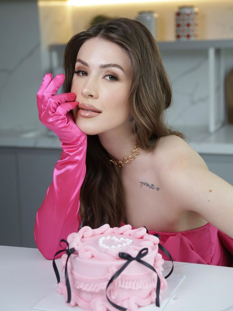Dani Choma de vestido e luvas rosas apoiada em balcão com bolo rosa 