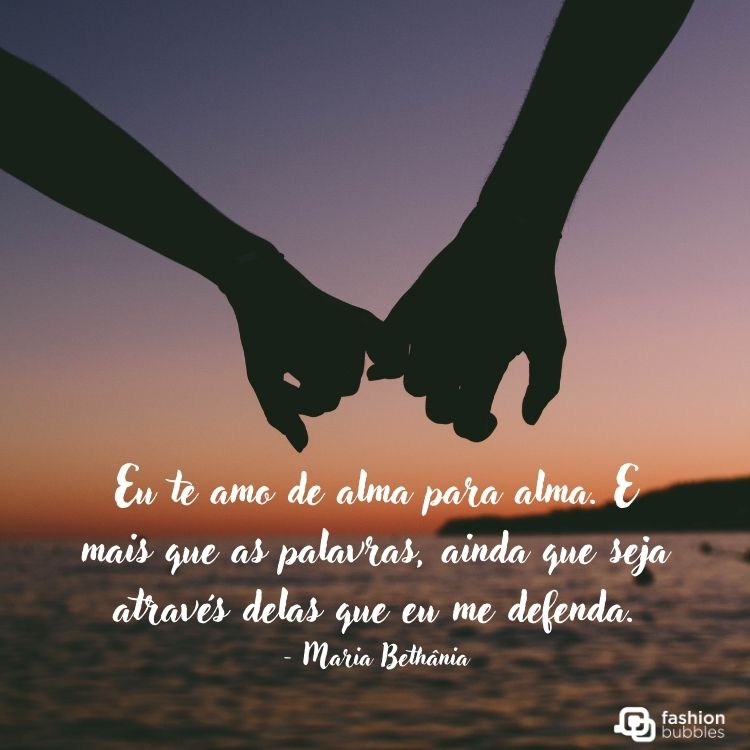 Duas pessoas de dedinhos entrelaçados na praia no pôr do sol e frase  “Eu te amo de alma para alma. E mais que as palavras, ainda que seja através delas que eu me defenda” - Maria Bethânia
