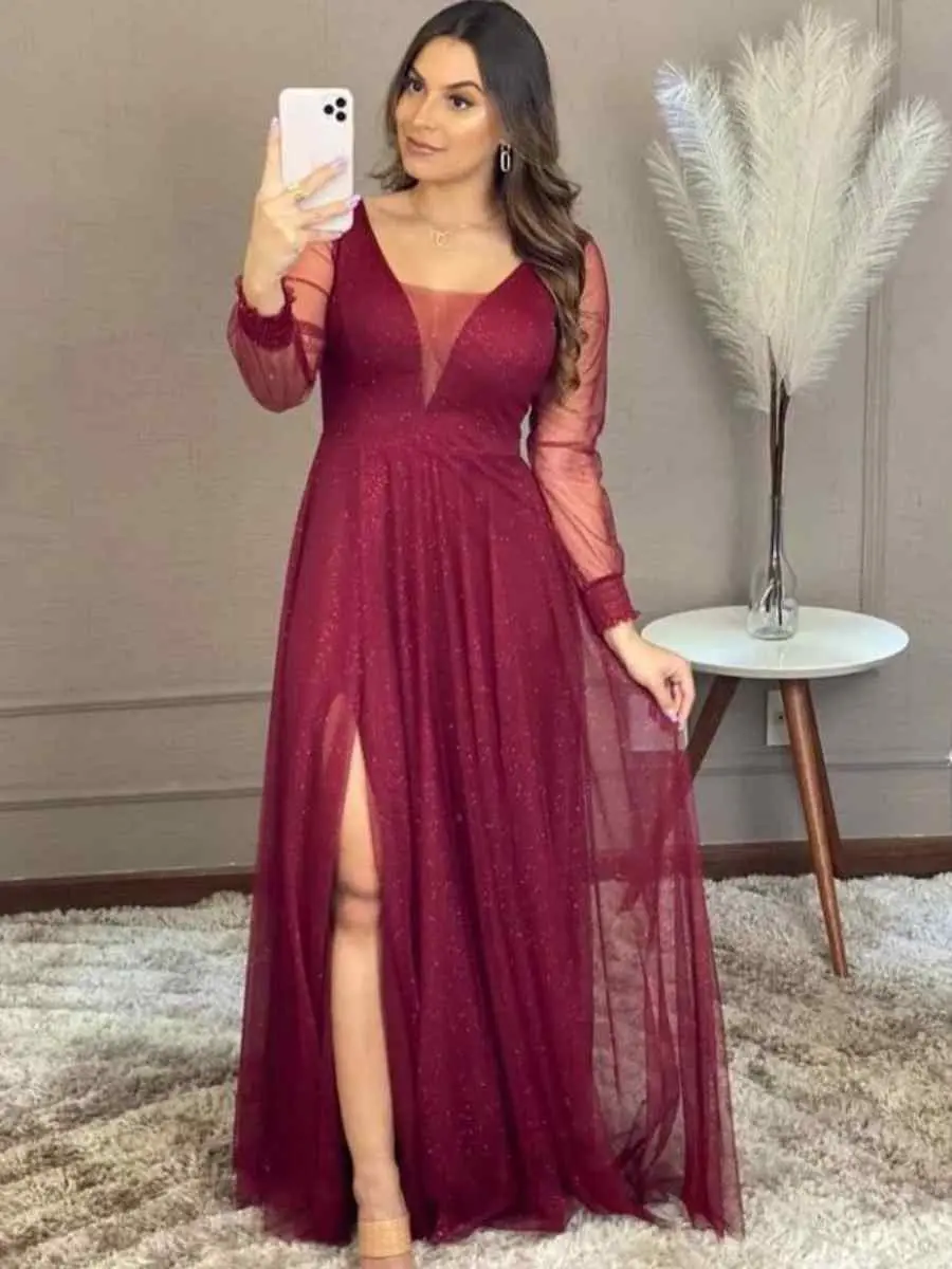 Mulher usando look vermelho-escuro para o Natal composto por vestido longo de fenda e tecido transparente.