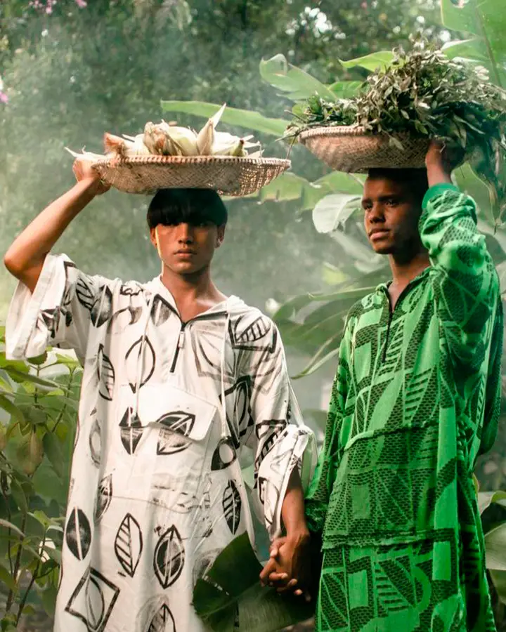 Casal de modelos, um usando branco o outro verde, de mãos dadas.