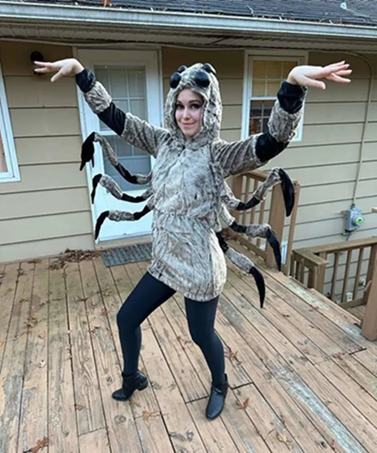 Mulher de pele clara usando fantasia de aranha marrom, com capuz e pernas, além de calça legging pretsa