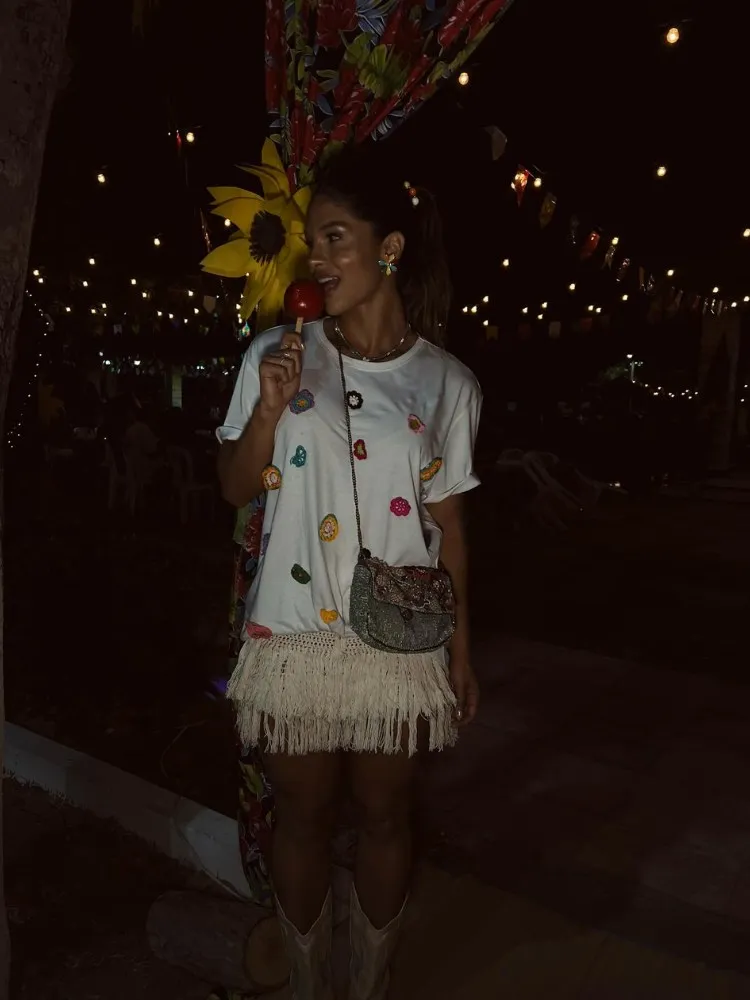 Mulher de pele clara de camiseta branca com flores bordadas, saia bege de macramê e bota western