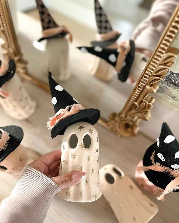 mulher segurando decoração de fantasma com chapéu de bruxa