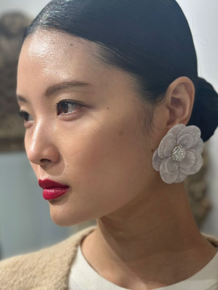 Mulher asiática usando maquiagem natural, batom vermelho, brinco de flor e cabelo preto em coque baixo