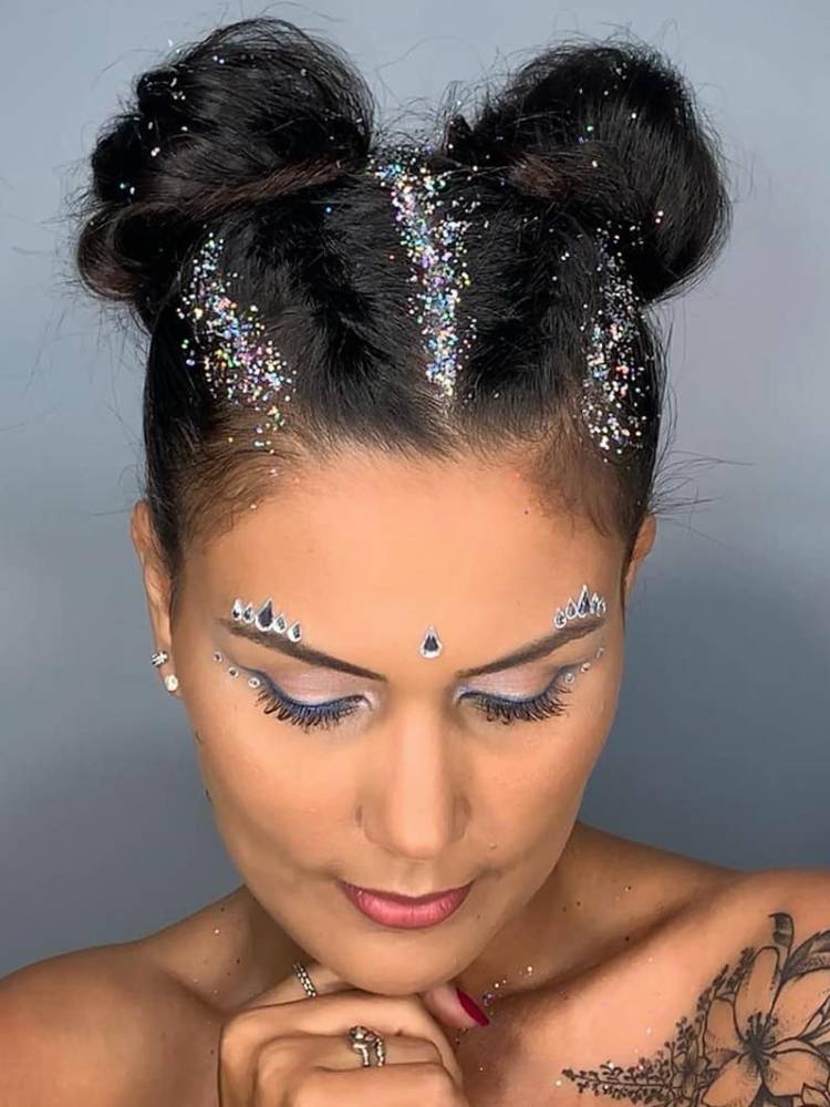 Mulher de pele clara com space buns e glitter. 