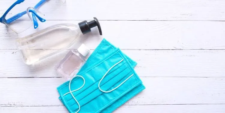 Álcool em gel, máscara descartável azul e óculos de proteção.