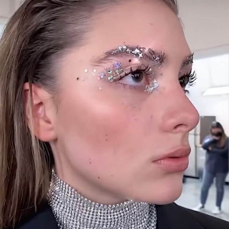 Mulher de pele clara com glitter e estrelas nos olhos, sobrancelha e canto interno