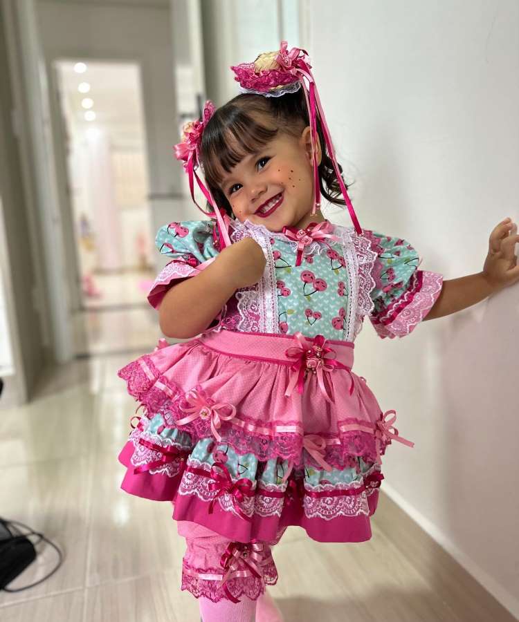 Garotinha com vestido rosa e verde com estampa de cereja e chapéus pequenos no cabelo