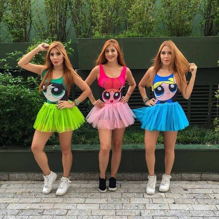 Três mulheres de pele clara e cabelo ruivo usando fantasias das Super Poderosas