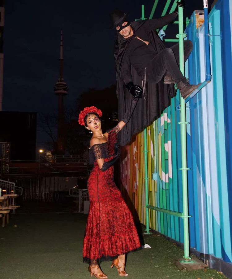 Mulher fantasiada de caveira mexicana e homem de zorro, com capa de Halloween