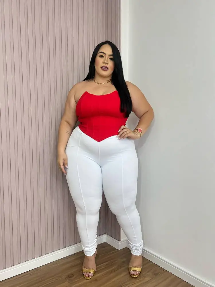 Mulher de pele clara e cabelo preto usando cropped corset vermelho e calça justa branca.