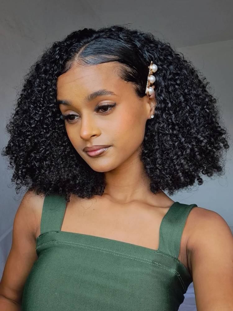 Mulher de pele negra usando blusa verde e cabelo cacheado preto preso com presilha de pérola