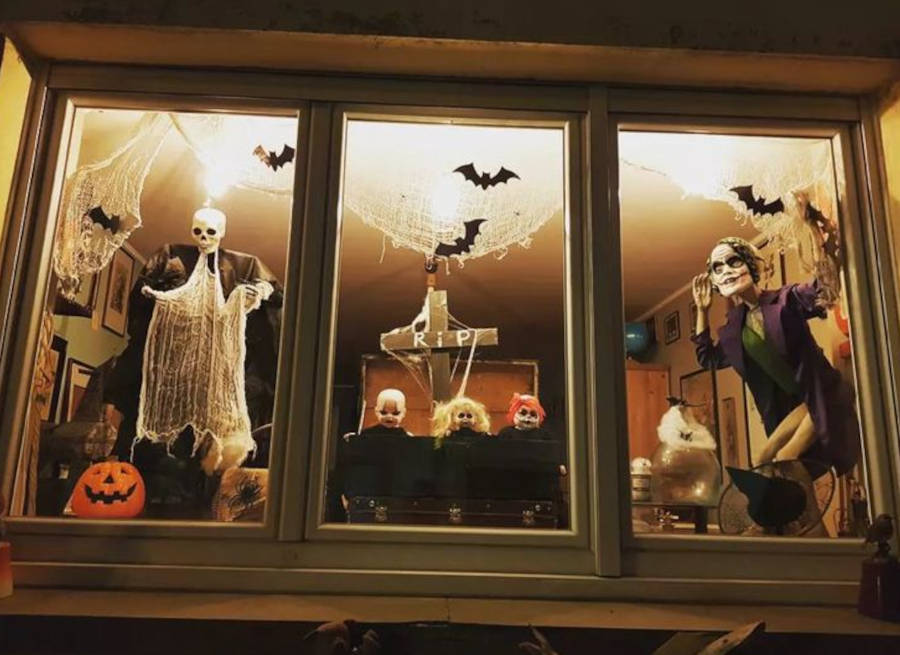 Foto de vitrine de Halloween com decoração com luminária e morcegos no vidro, além de caveiras e bonecos assustadores