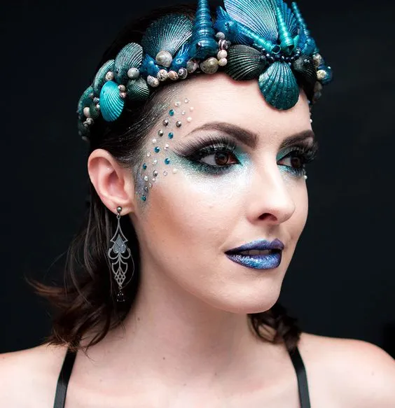Mulher de pele clara com maquiagem de sereia em tom azul e coroa de sereia com conchas azuis