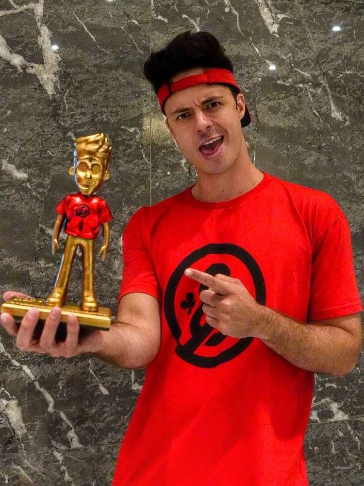 Enaldinho com blusa vermelha de sua marca e segurando seu boneco dourado