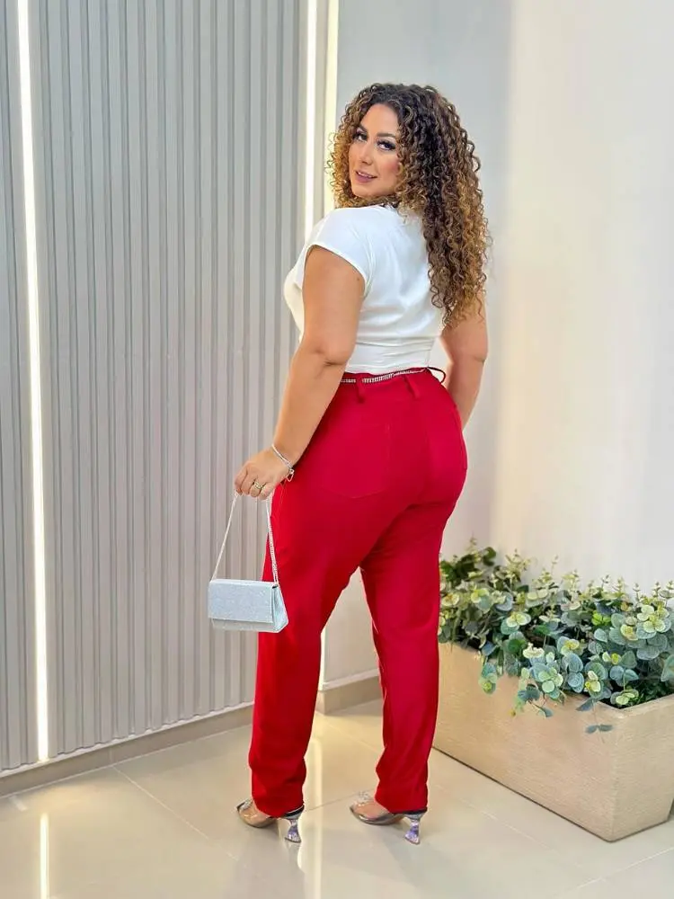 Mulher de pele morena e cabelo cacheado usando blusa branca e calça vermelha justa.
