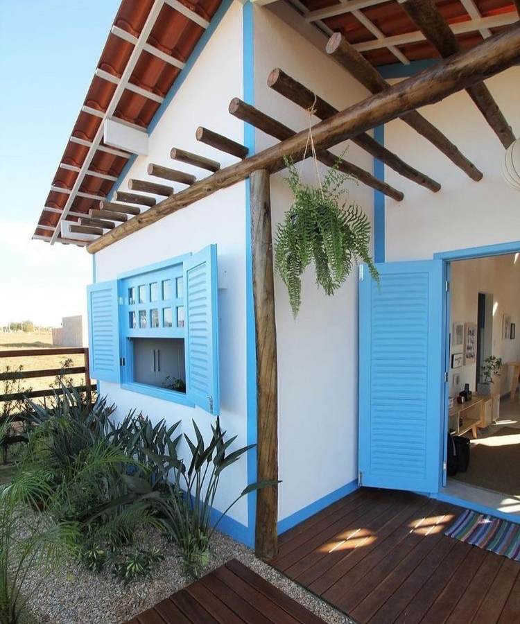 Entrada de casa rural branca e azul com pergolado e planta samambaia pendurada