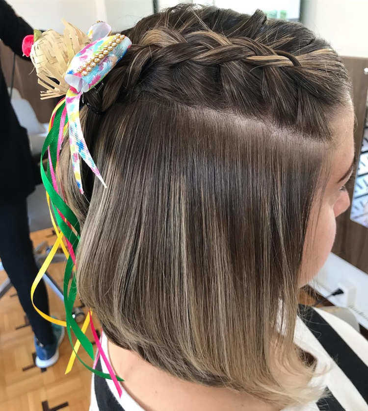 Mulher com cabelo curto e trança lateral. Ela tem um adereço de festa junina na trança.