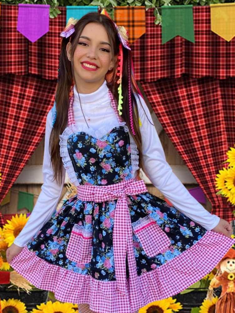 Mulher de pele clara de blusa manga longa branca com avental junino preto com flores e detalhes em xadrez vermelho 
