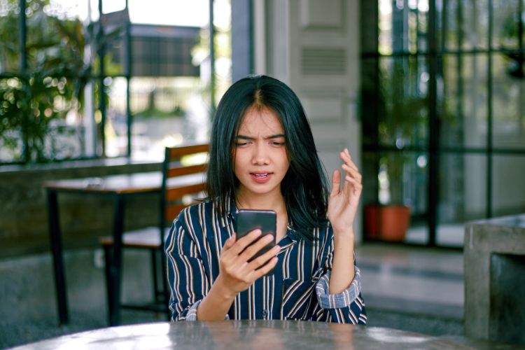 Pessoa segurando celular em uma mesa com expressão confusa