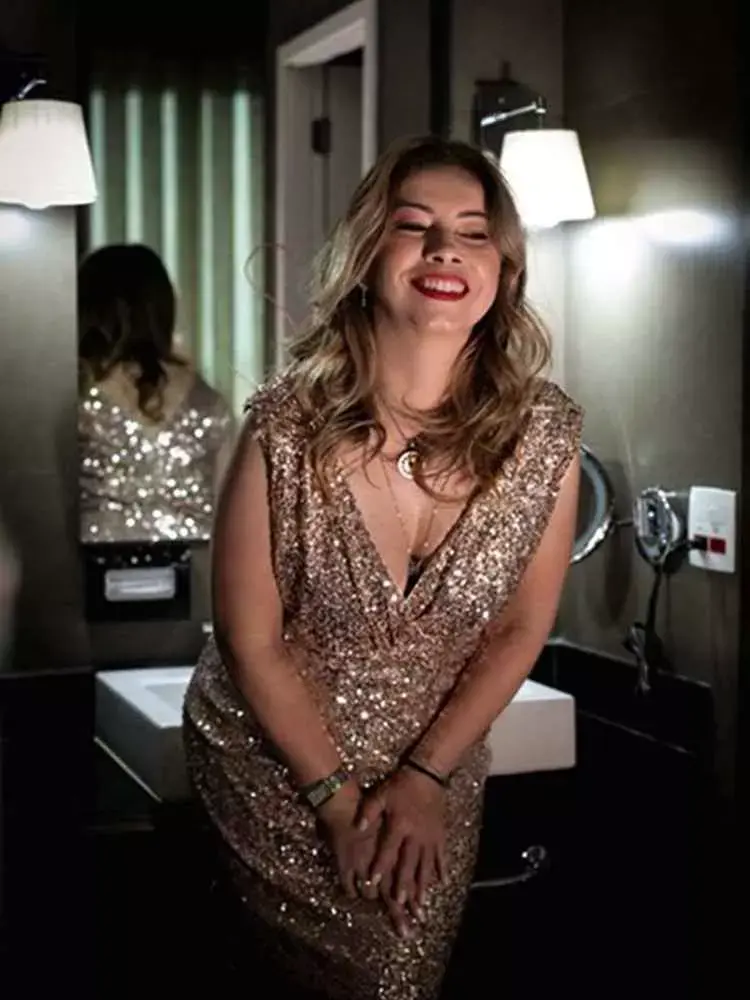 Mulher não-modelo com mais de 40 anos em ensaio fotográfico, usando vestido de paetês dourado, em banheiro