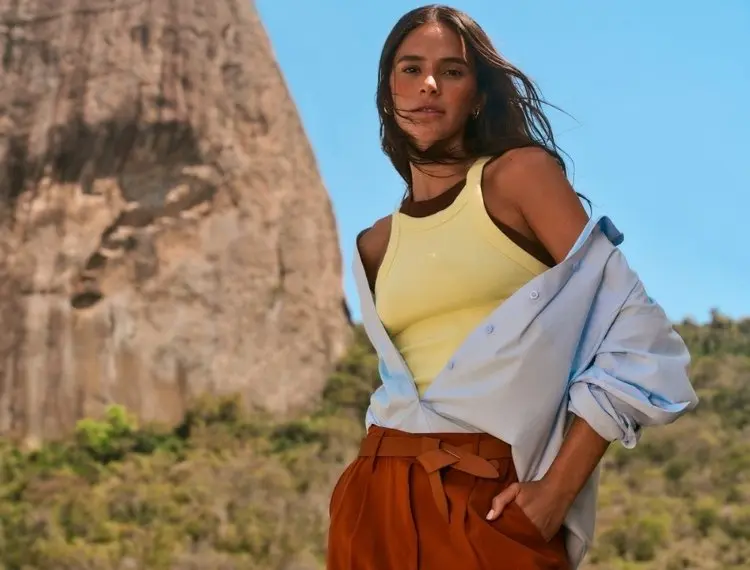 Foto de Bruna Marquezine de regata amarela, camisa azul e calça marrom na campanha de verão 26 da Hering