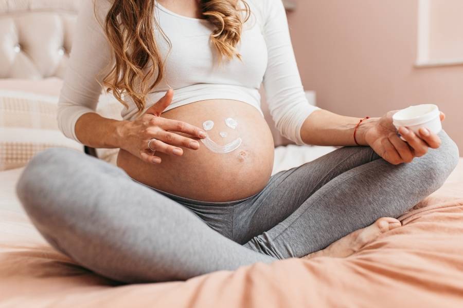 Mulher com gestação tardia passando creme na barriga.