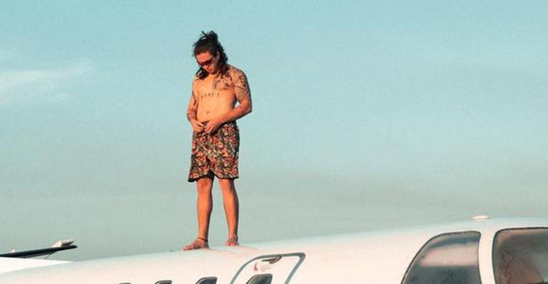 Whindersson Nunes aparece em cima de seu jatinho. Ele usa apenas bermuda dlorida e óculos de sol, céu azul ao fundo, Whindersson Nunes sobe em jatinho de 1,4 milhão