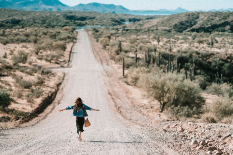 Foto de mulher de braços abertos em estrada de terra, simbolizando a jornada para desenvolver a espiritualidade