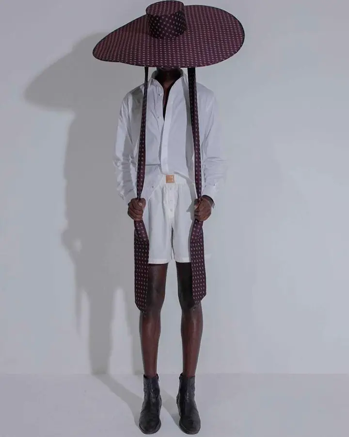 Modelo com blusa branca de botões e chapéu grande de cor escura.