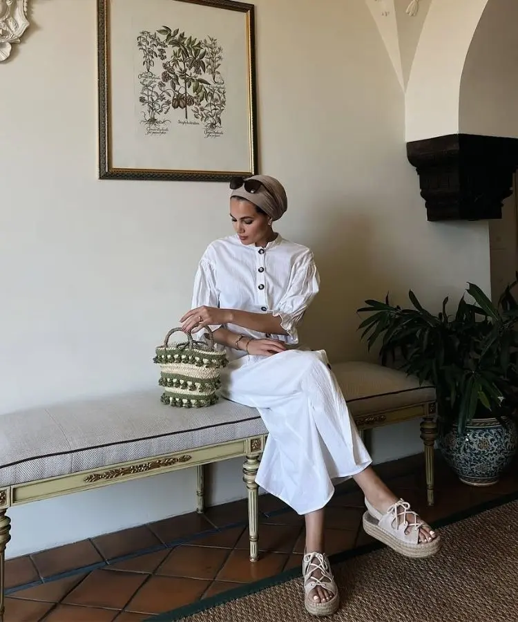 Mulher usando look branco com papete de palha nos pés, uma das tendências de sandálias para o verão 2026