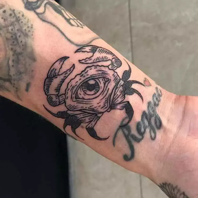 tatuagem no pulso de caranguejo com olho grande no centro e outras tatuagens ao redor 