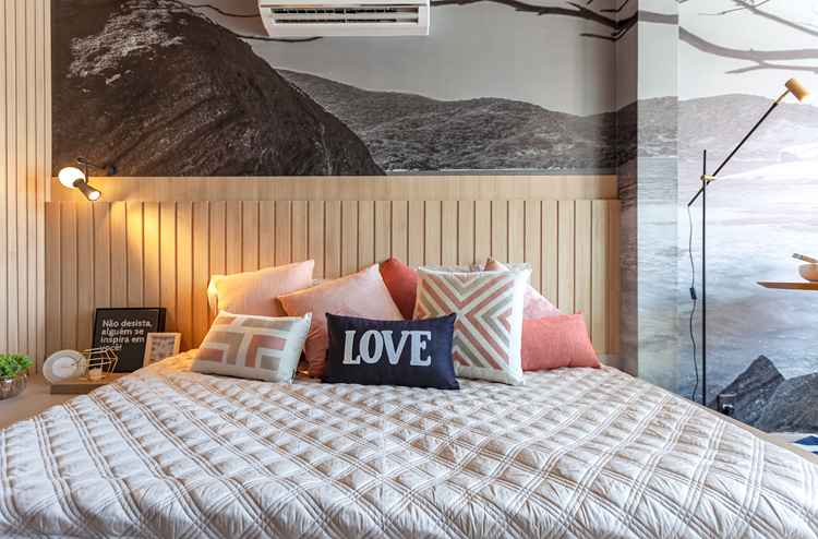 foto de cama de casal em quarto decorado, com papel de parede de paisagem, cabeceira de madeira e almofadas na cama 
