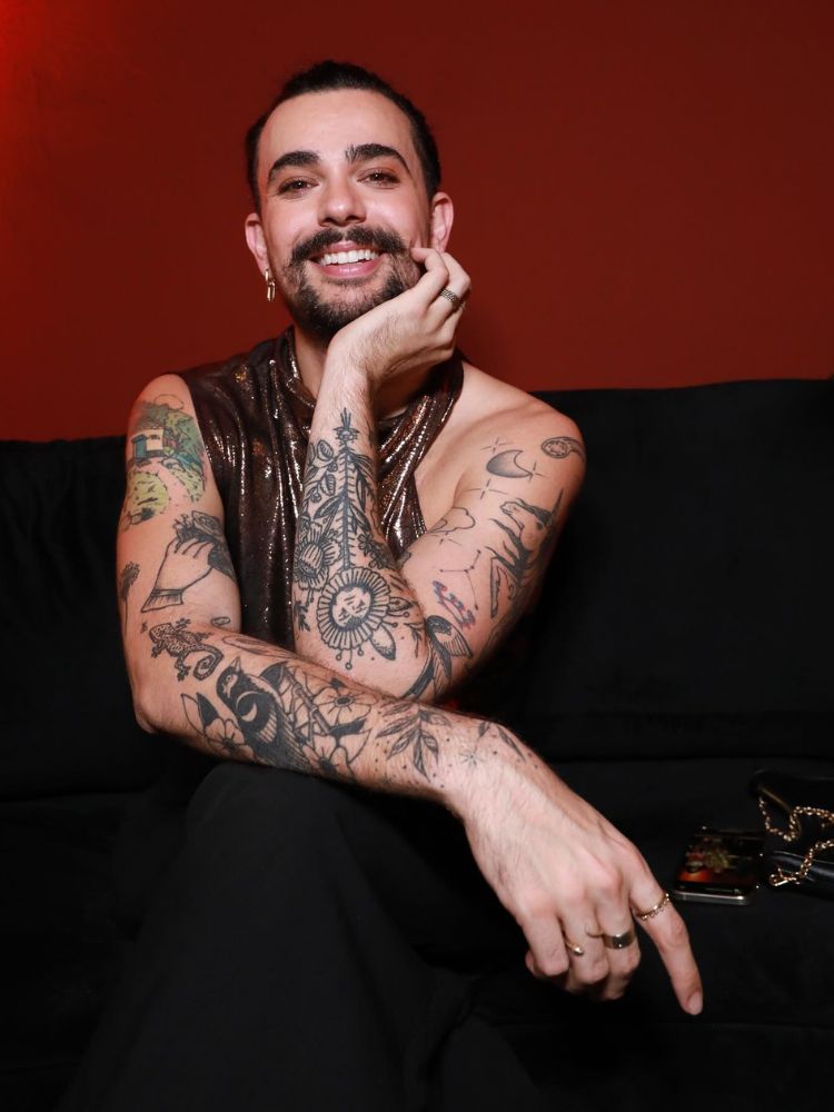 Vitor DiCastro de blusa dourada e calça preta sentado em sofá preto 